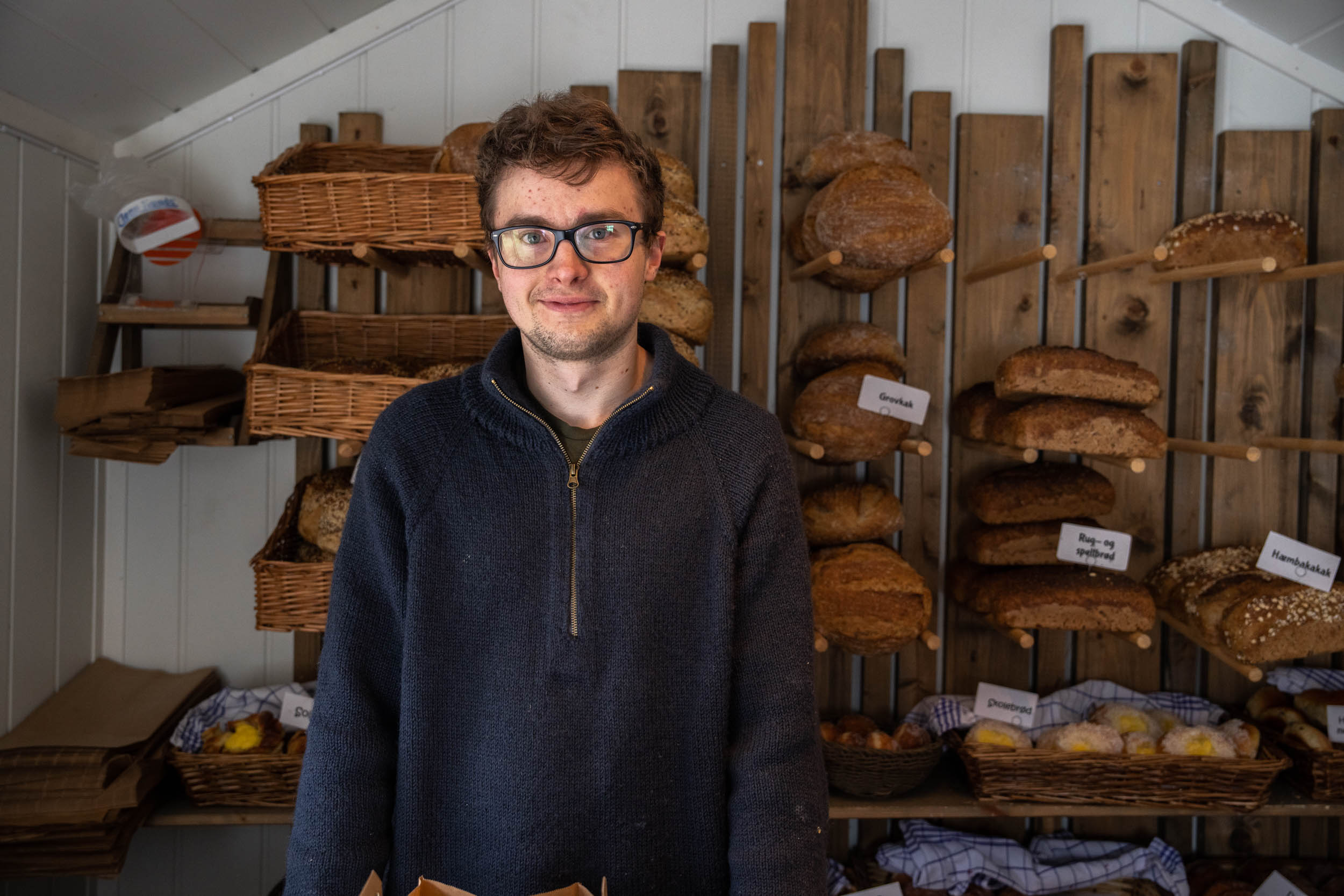 Mann smiler, hyller med brød i bakgrunnen, foto