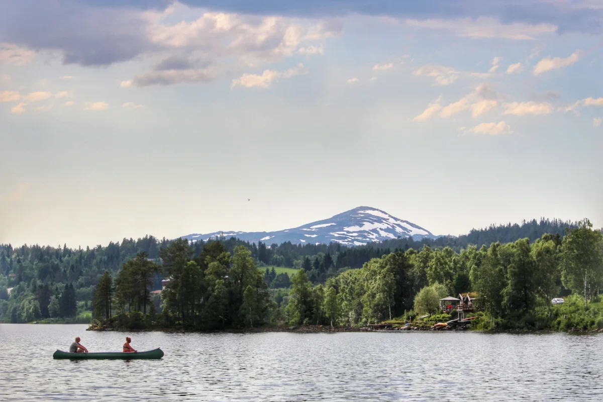 To personer i en kano på vannet, fjell i bakgrunnen, foto