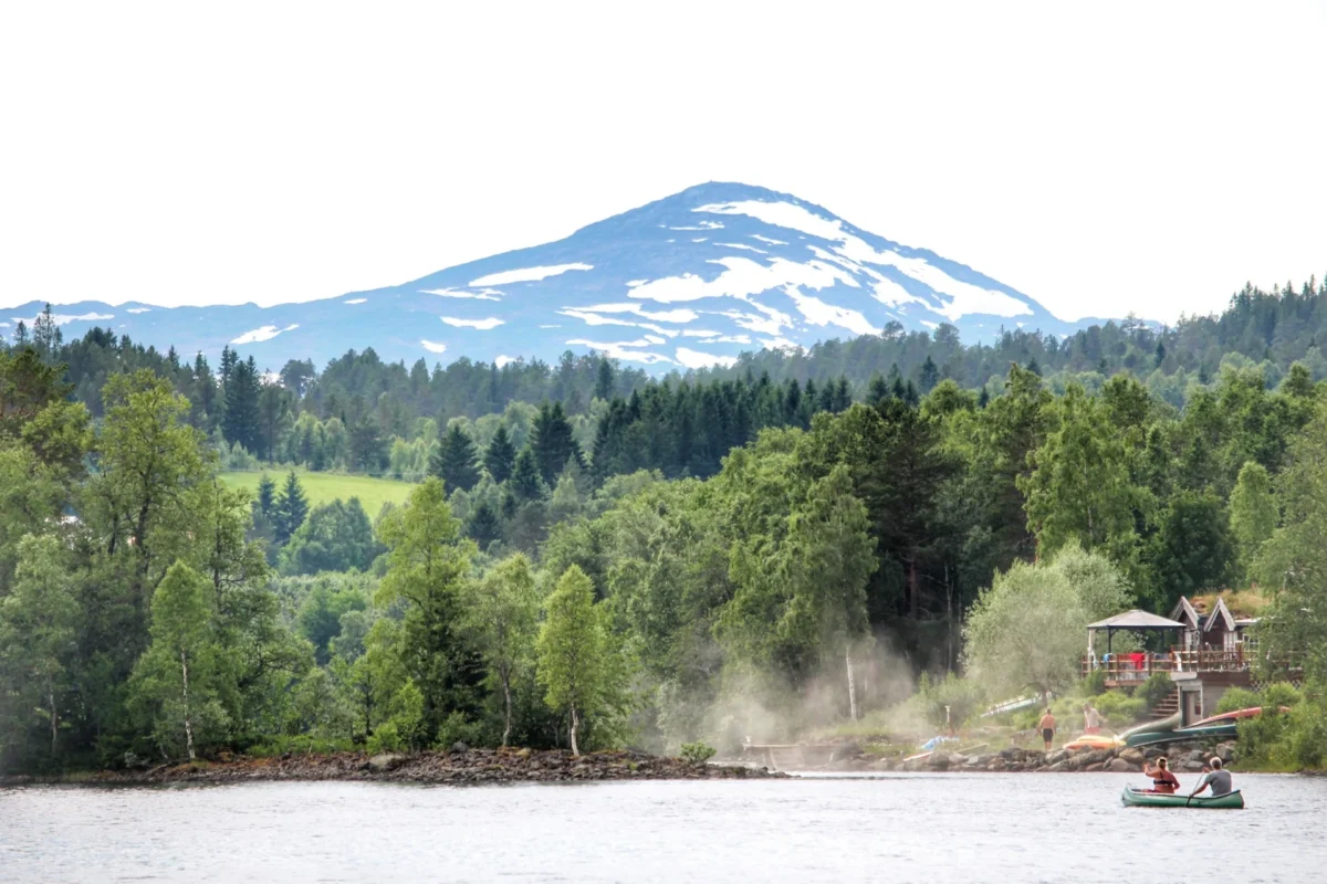 To personer i en kano på vannet, fjell i bakgrunnen, foto