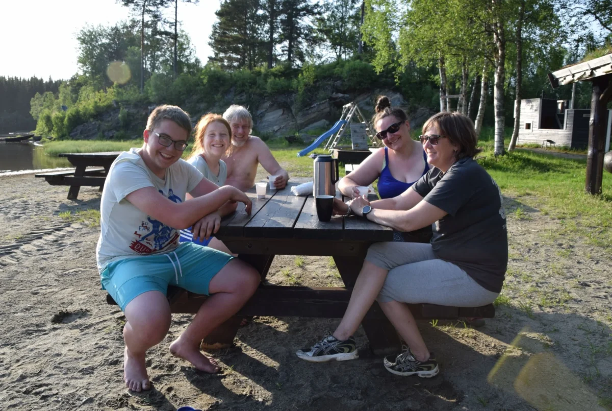 Fem personer sitter rundt et bord og smiler, foto