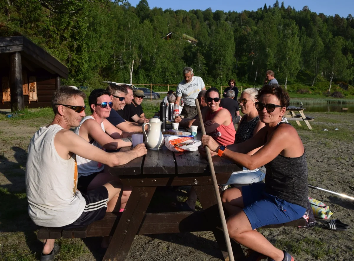 Flere personer sitter rundt et bord i solskinnsvær, foto