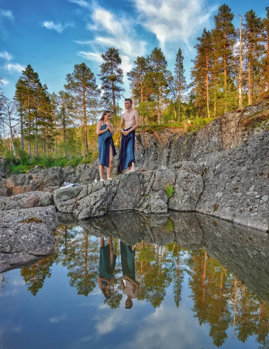 To personer står med håndduker ved elva, foto