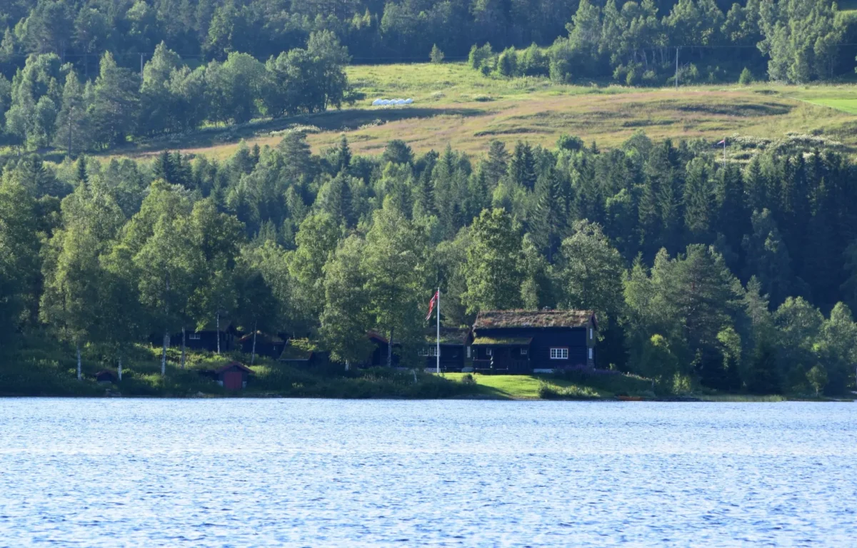 Hytte med trær rundt og vann i forgrunnen, foto