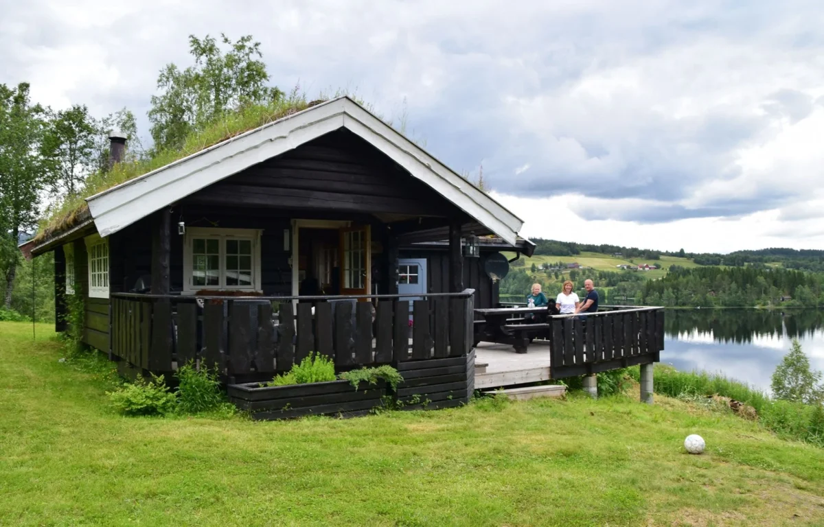 Hytte, familie sitter på terassen, vannkanten like bak, foto