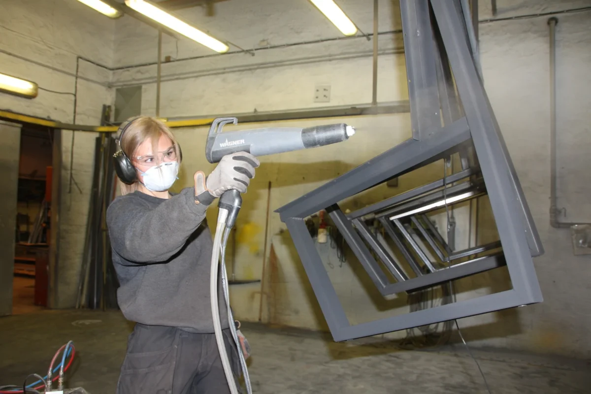 Lærling i verneutstyr sprayer metall, foto