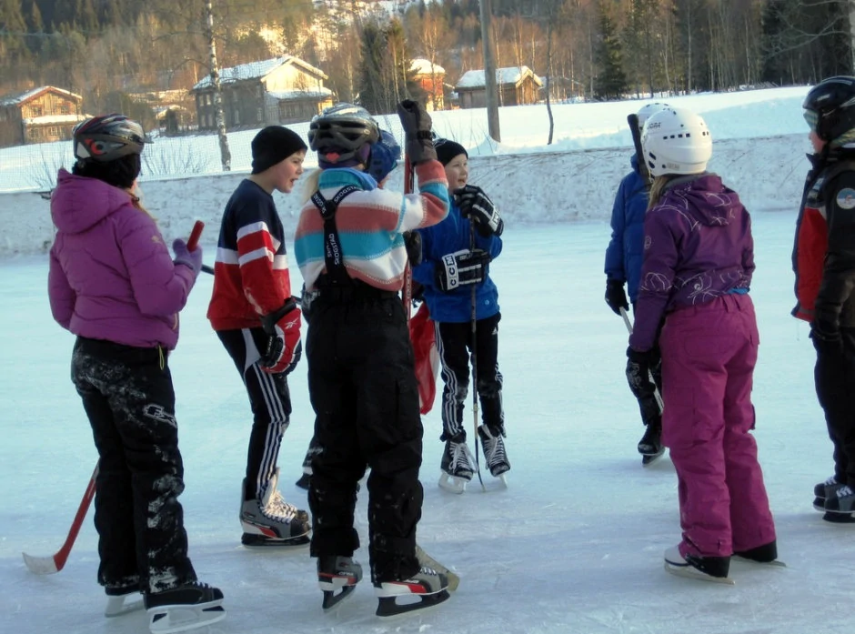 Barn står på ishockeybanen og prater sammen, foto