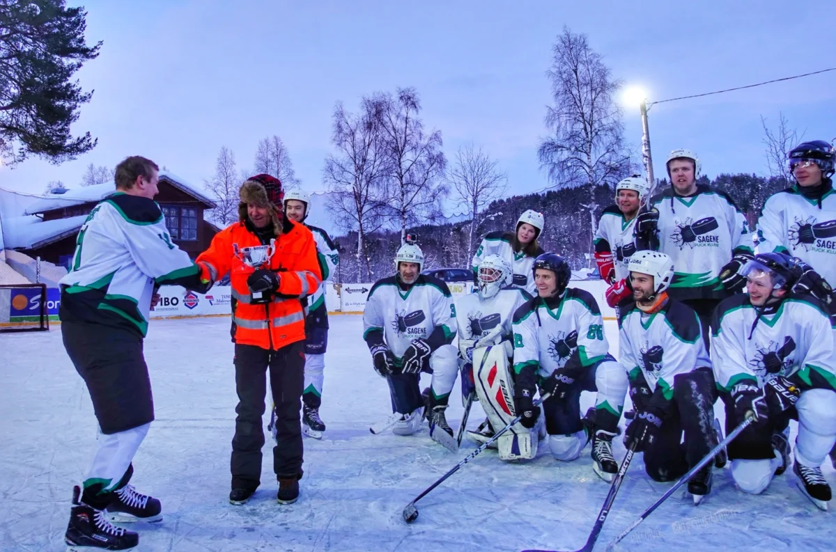 Mann får utdelt en pokal, ishockeylaget står og ser på, foto