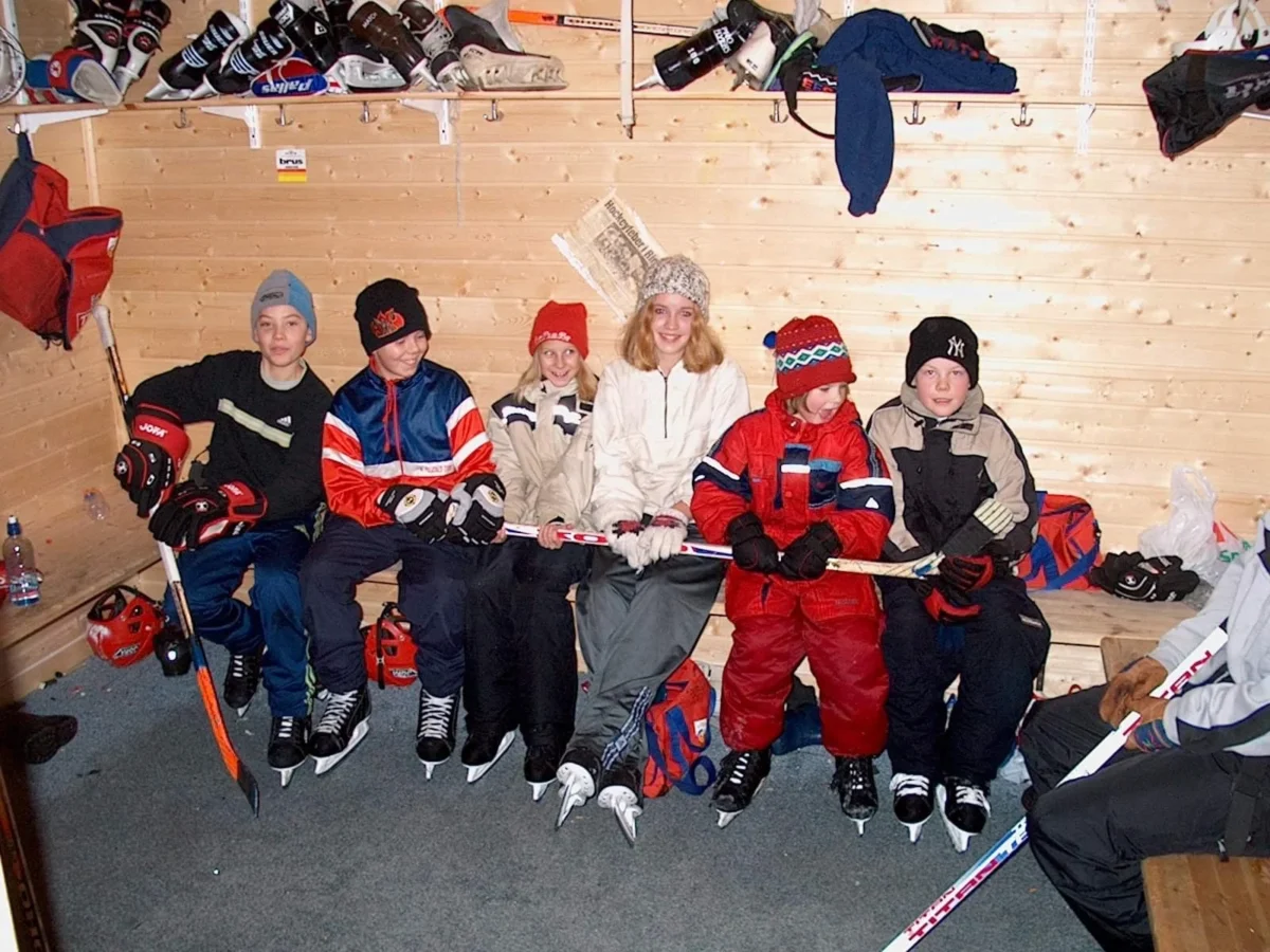 Barn med ishockeyutstyr sitter i varmestue, foto