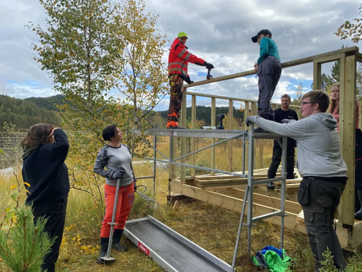 En voksen ser på at elevene bygger båthus, foto