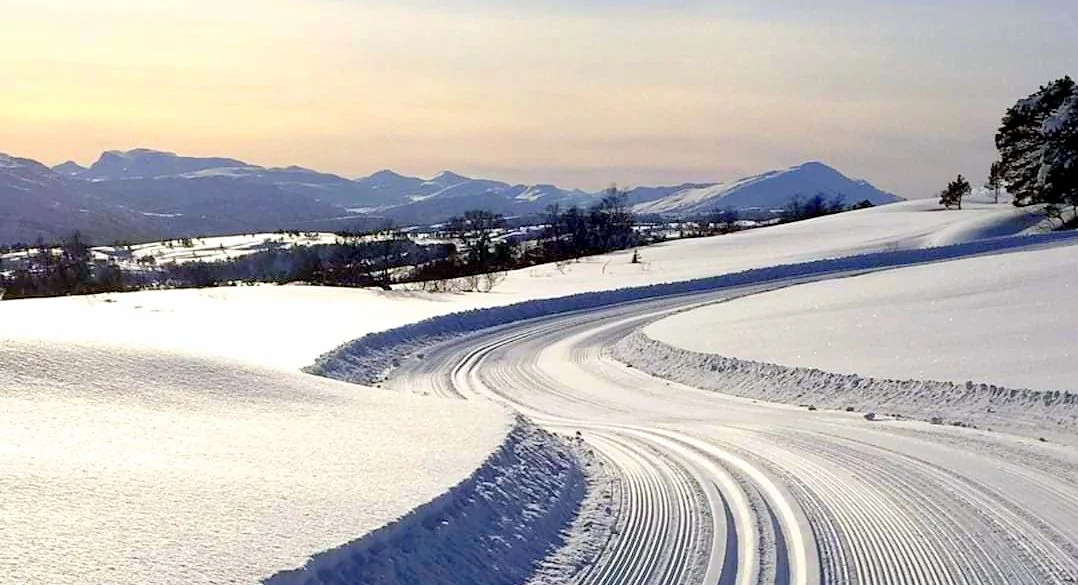 Skiløype i snøen som svinger seg, fjell i bakgrunnen, foto